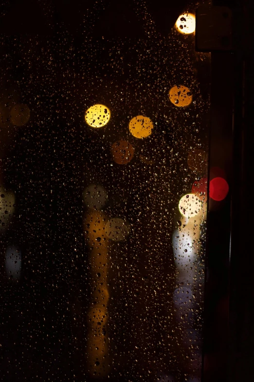 rain drops are seen on a window, some lights and street signs