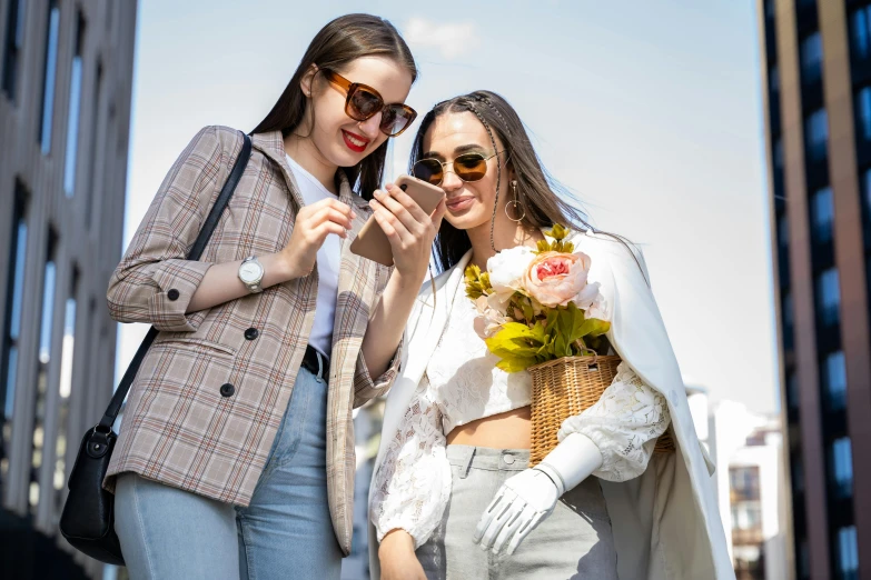 two women standing outside, looking at a cell phone