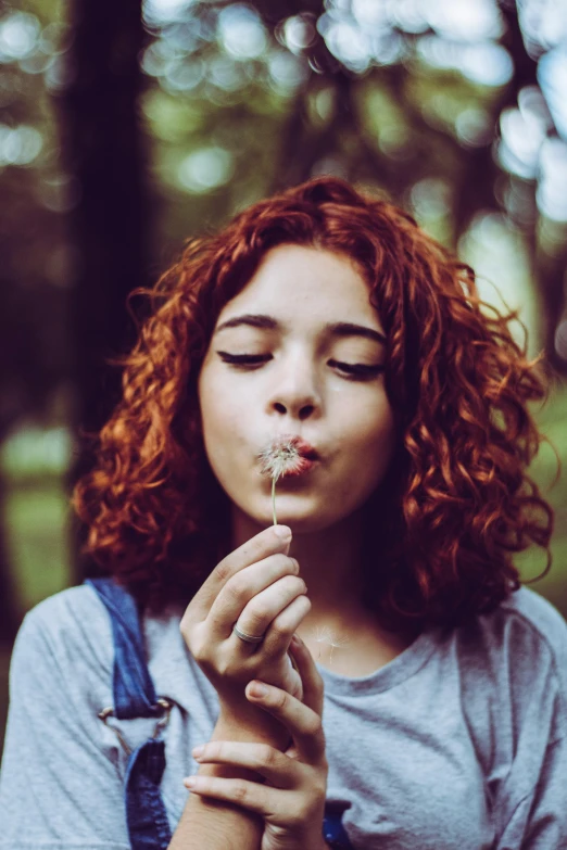 woman blowing dandelion by her face in the woods