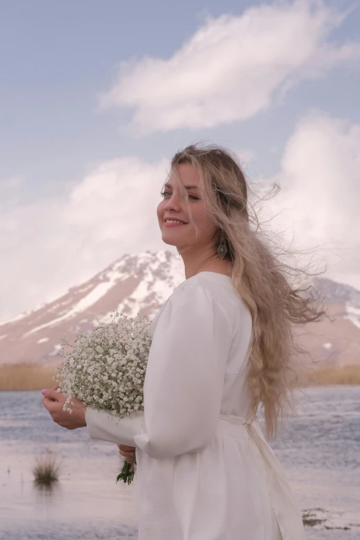 there is a woman standing on the shore of the water holding flowers