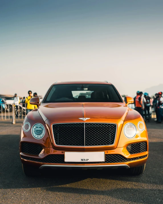 a brown bentley sits parked in front of a crowd