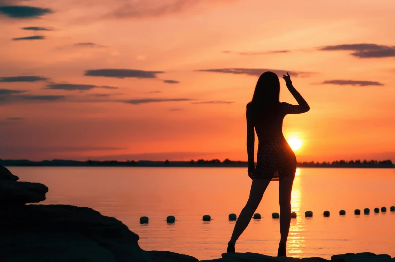 a woman in black bathing suit standing near water at sunset