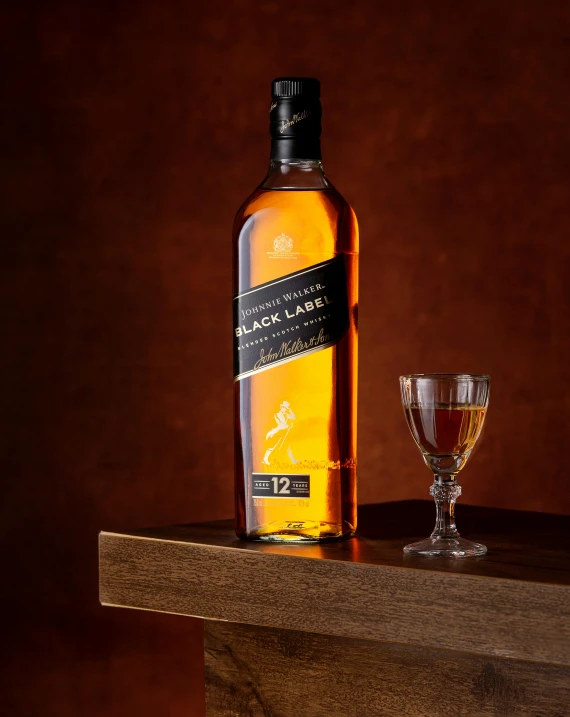 a glass of liquid and bottle of whisky on a wooden shelf