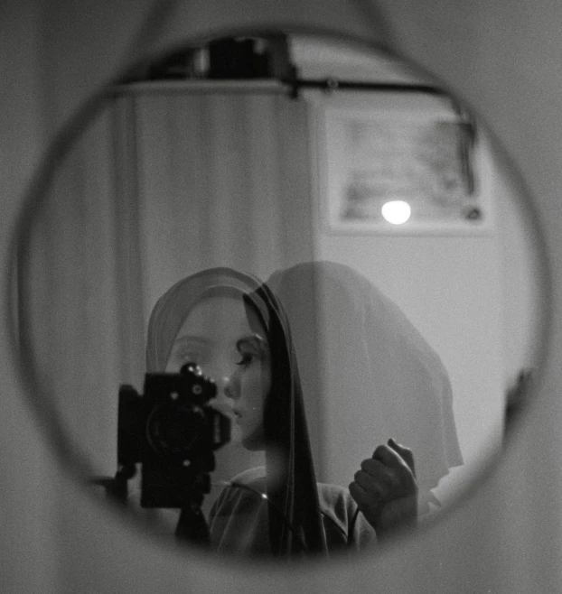 a woman is holding a camera and looking through a mirror