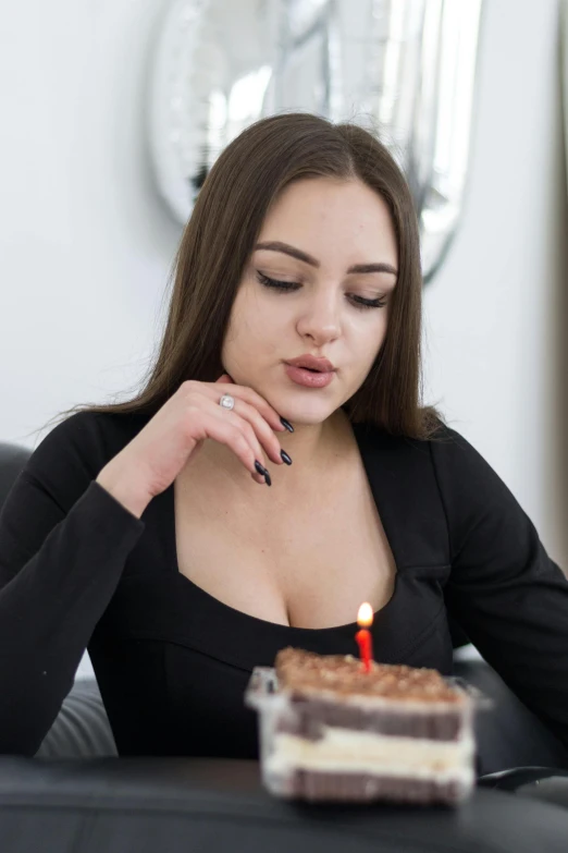 woman blowing out candle on chocolate cake with brownie