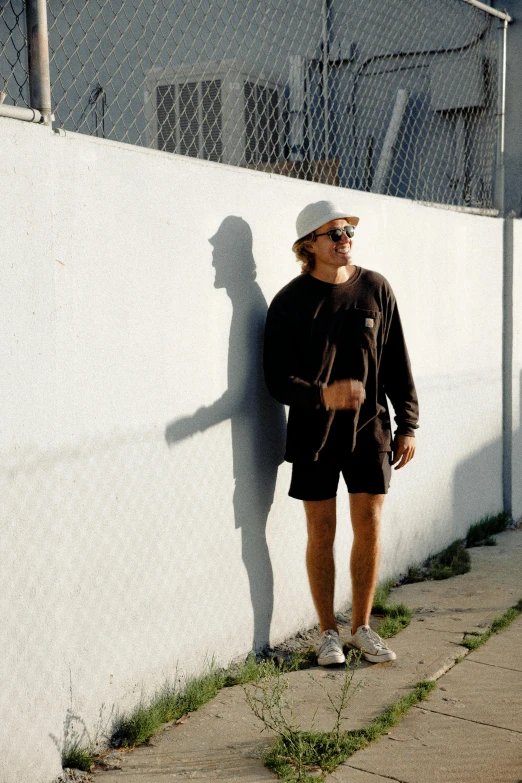 a man stands against a wall next to his skateboard