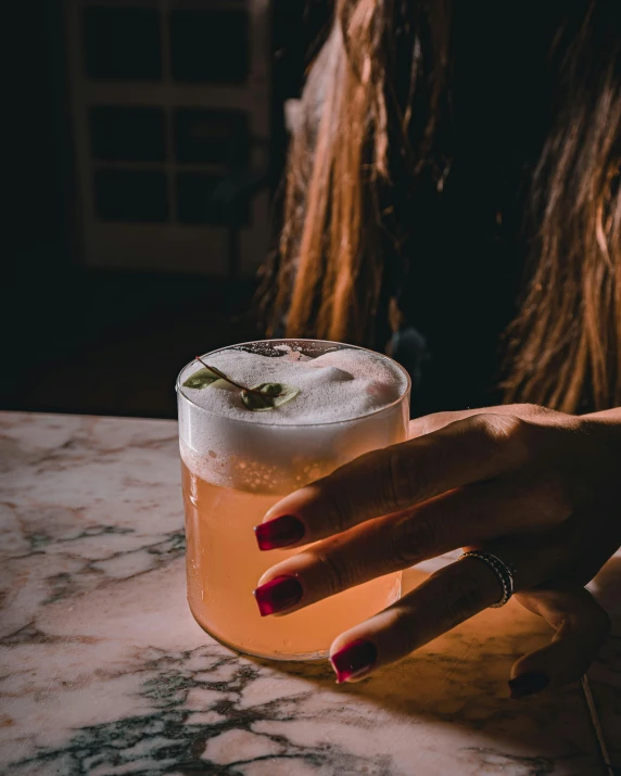 someone holding onto a cocktail glass with a small green flower on top