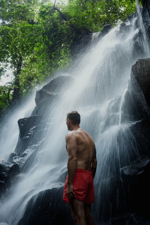 young man standing in front of a waterfall while wearing red boxers