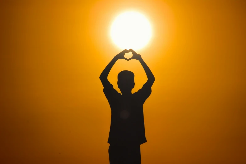 silhouette of a man with heart shaped hands in the sun