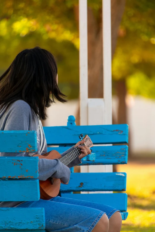 a woman sitting on a bench playing an acoustic guitar