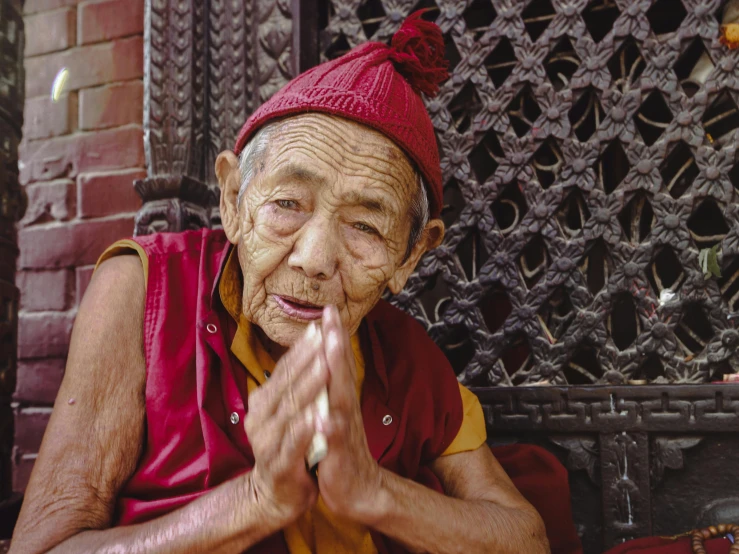 an old man in a red and yellow outfit sitting with his hands folded