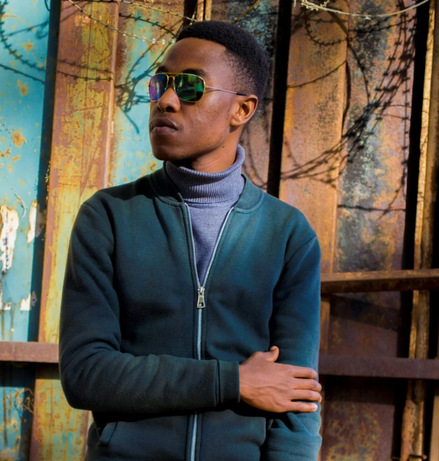 a man wearing sunglasses leaning against a rusty wall