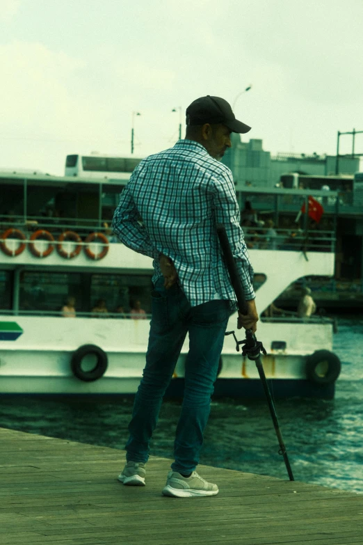 a man with a cane and a baseball cap is looking over a dock at a boat