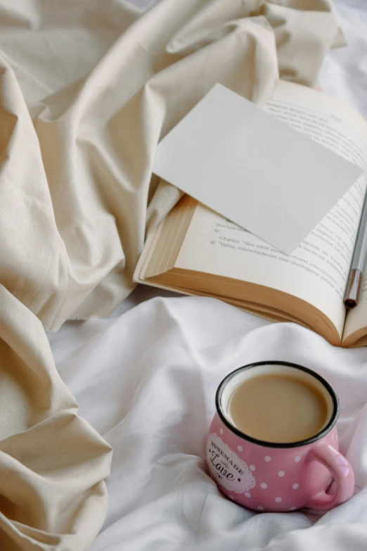 an open book and cup of coffee sit on top of a bed