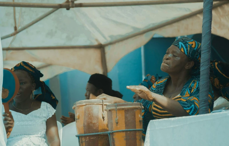 an older woman drumming with other young women in a tent