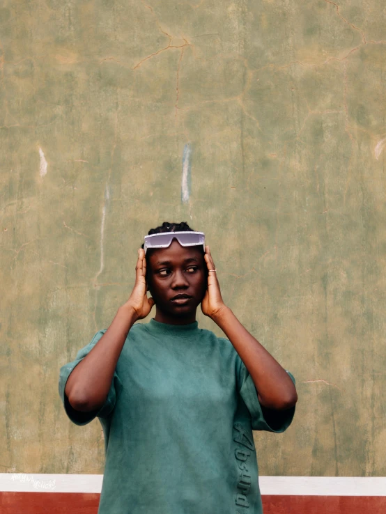 a woman standing in front of a green wall with her head tilted in two places with one hand on the top of her head