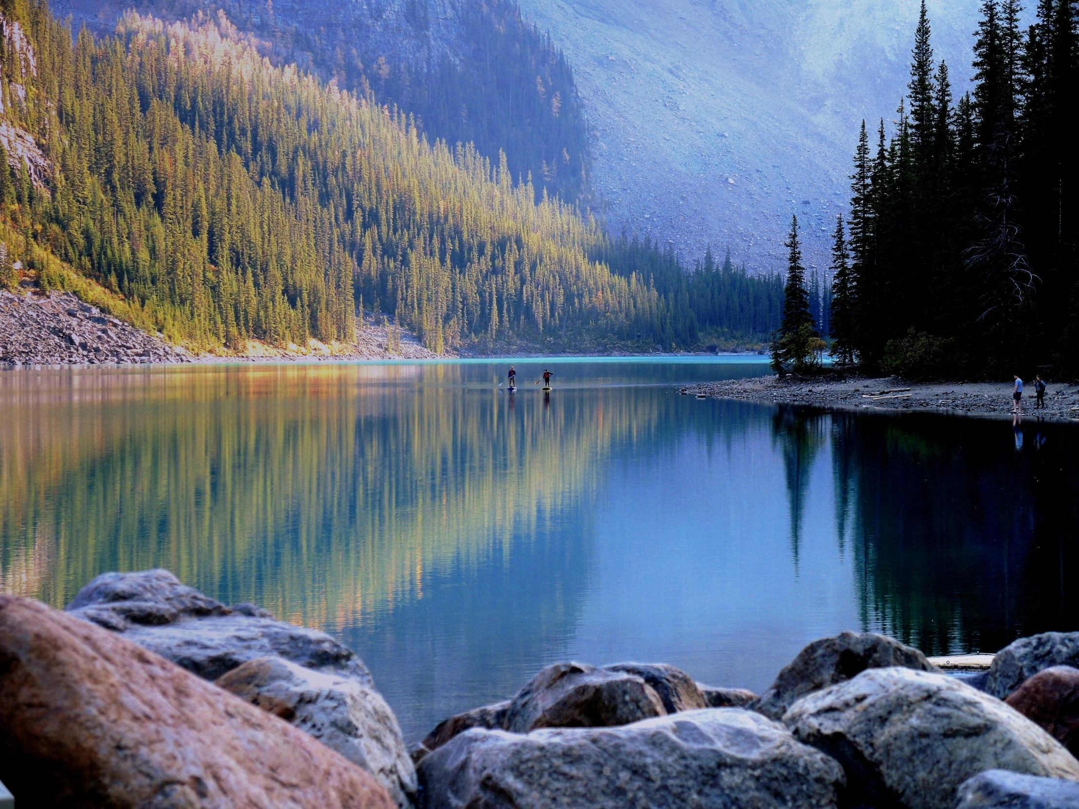 a body of water with rocks, trees and mountains