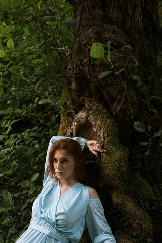 a woman in a blue dress sitting next to a tree