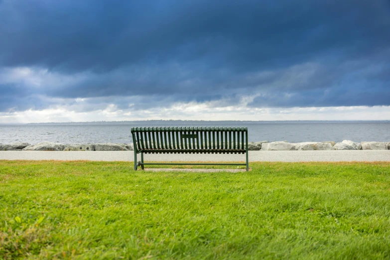 there is a bench by the ocean under a cloudy sky