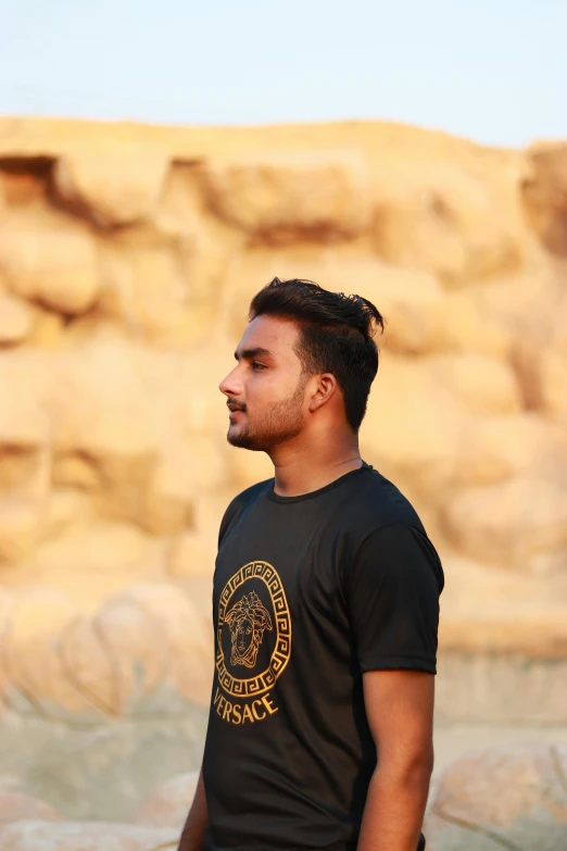 a young man in black shirt standing in front of a stone rock formation