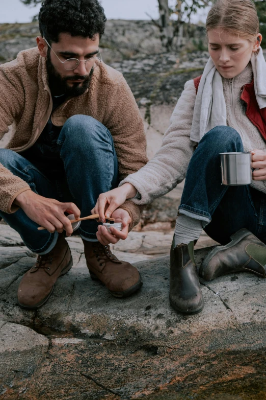 a man and woman sit on the edge of rocks holding a small cigarette