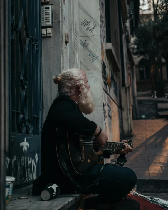 a man with a long hair sitting on the ground playing guitar