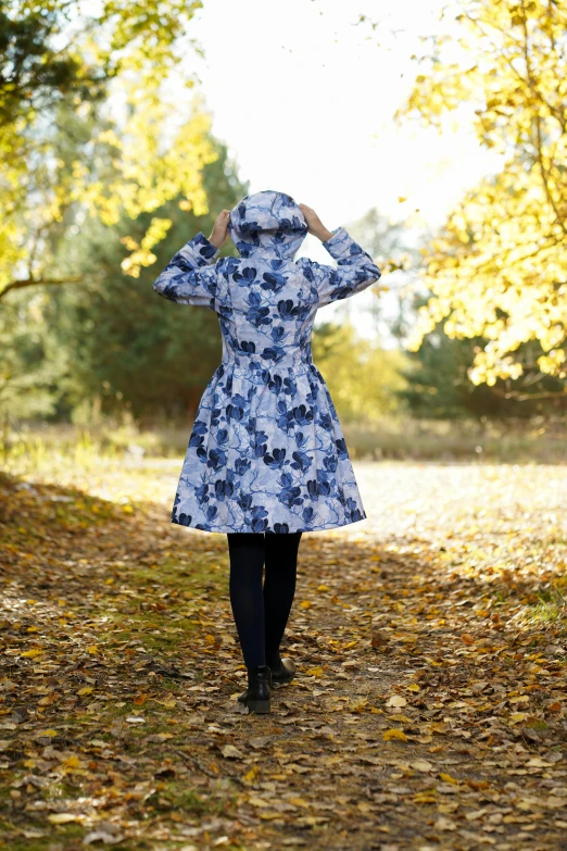 a woman in a dress is walking on a leaf covered path