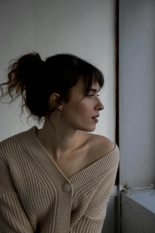 a woman in beige sweater standing near a window