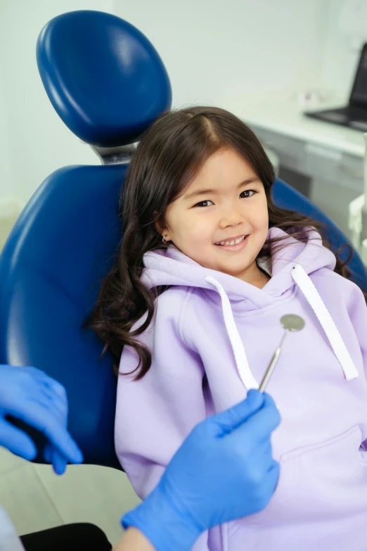 a girl sits in a dentist chair smiling at the camera