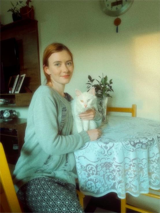 a young woman holding a white cat sitting at a table