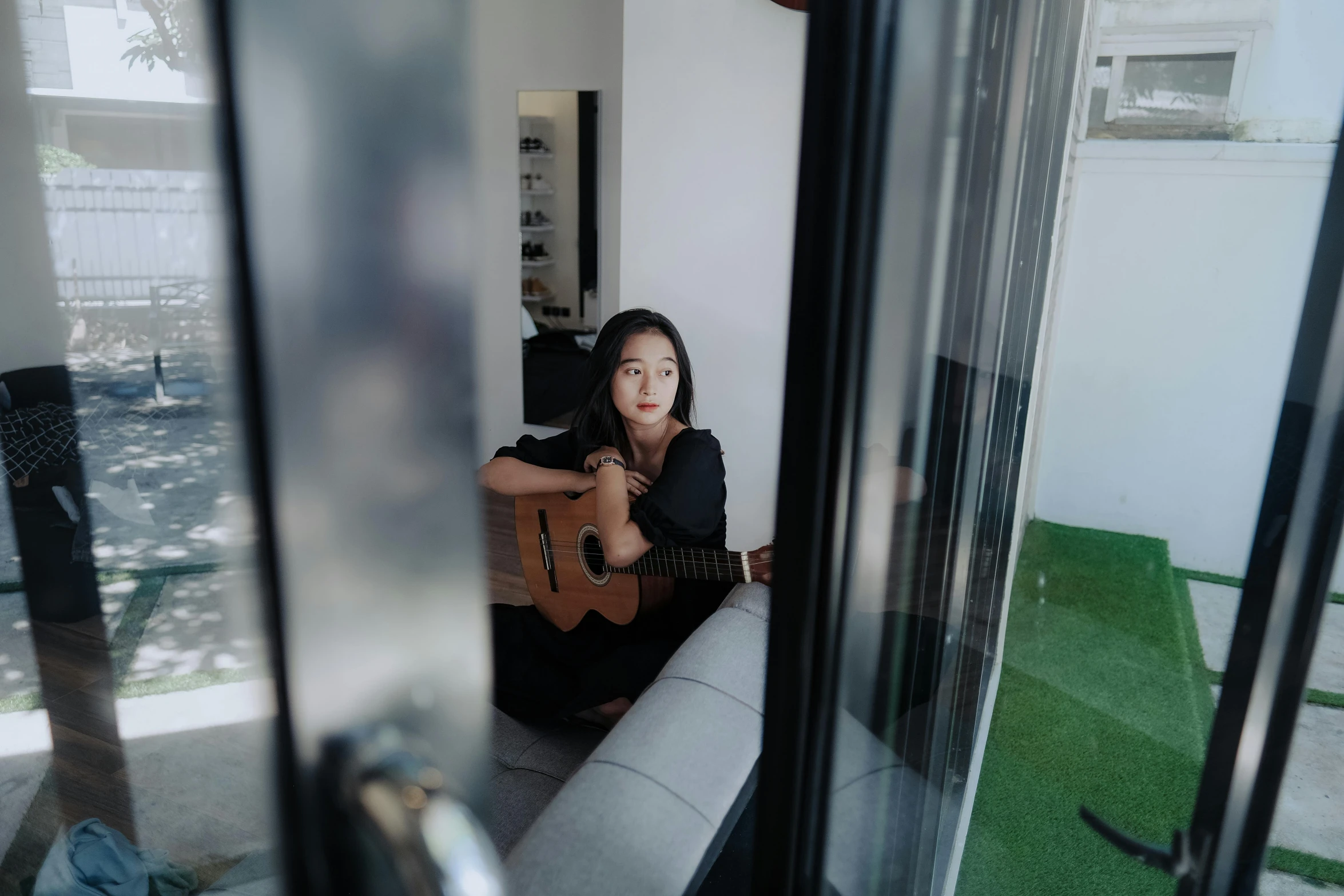 woman sitting on sofa playing guitar next to open door