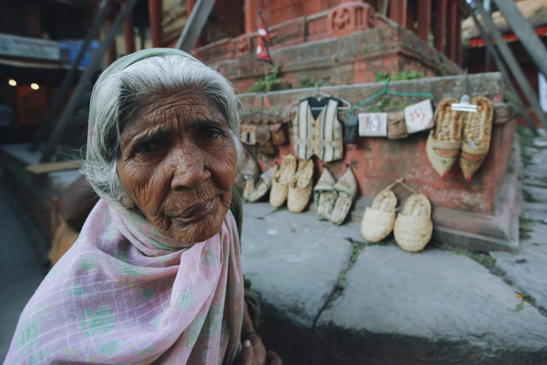 an elderly woman standing in front of a wall with many shoes and cloths