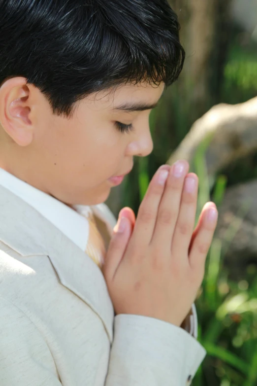 boy wearing suit and white shirt praying outdoors