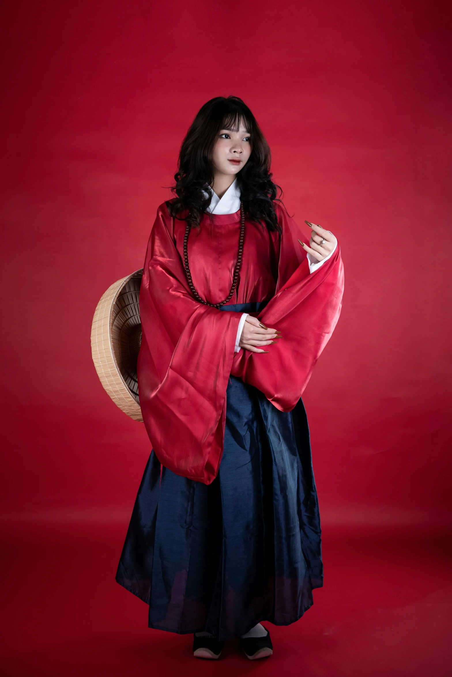 an asian woman with long hair wearing a red robe and holding onto a hat