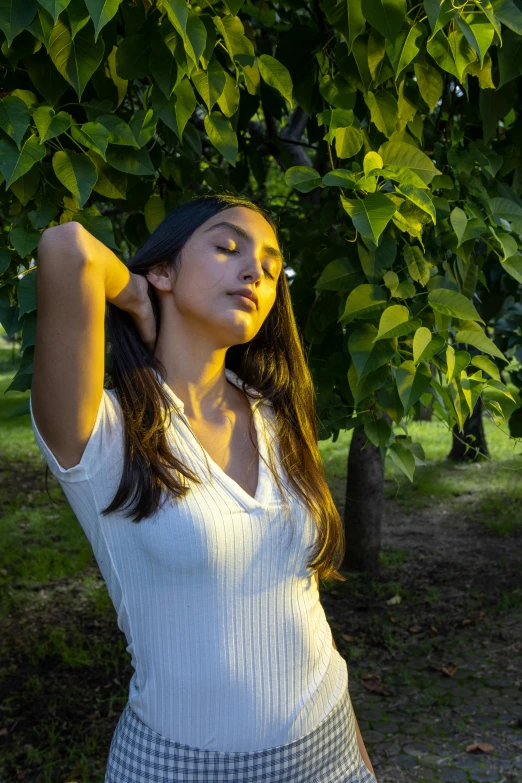 a woman is standing under the green leaves of a tree