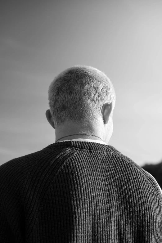 a man in a sweater looks out to sea from behind