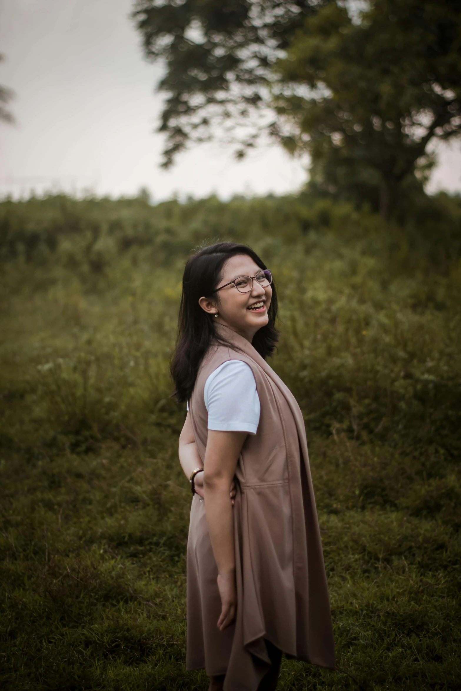 a woman standing in the middle of a grassy field with trees and bushes