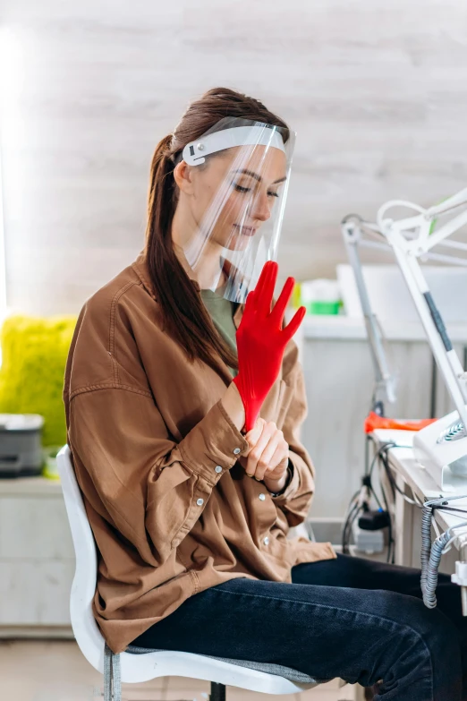 a woman sitting in a chair wearing a face shield and gloves