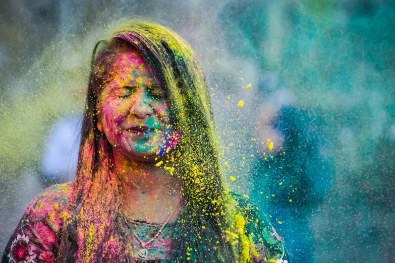 a woman in colorful holi powder pouring over her face
