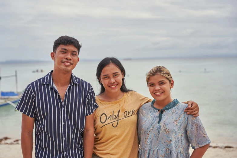 two young men and a woman standing in front of the ocean