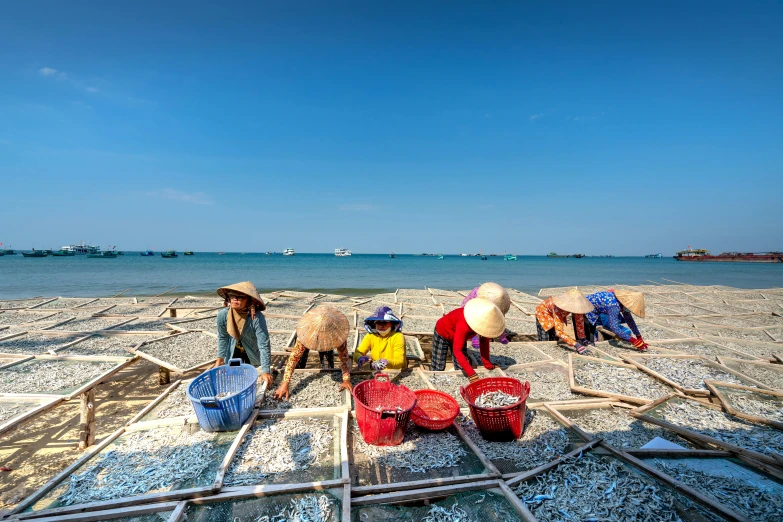 women sit on the beach near some buckets