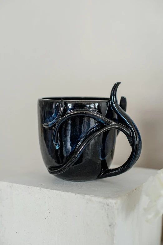 black coffee cup with curved handles sits on display