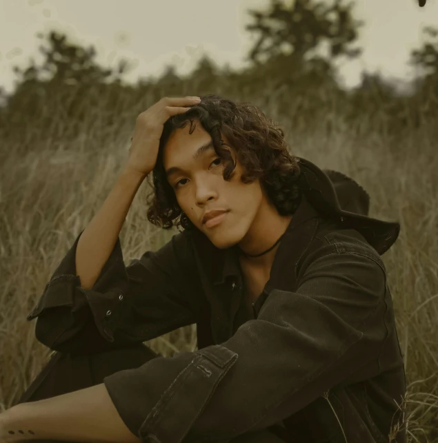 a male in a black jacket is sitting down in the grass