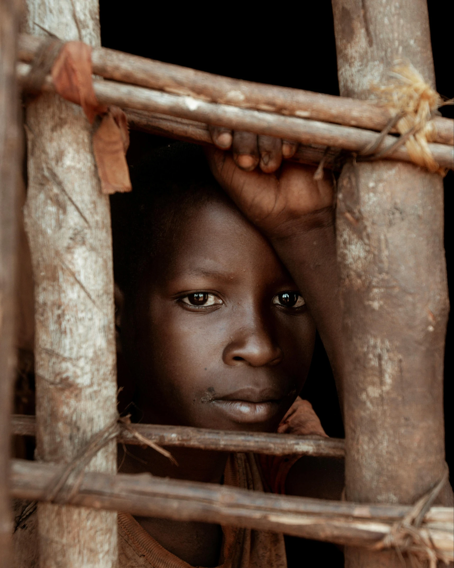 a child stands behind an old fence and looks into the camera