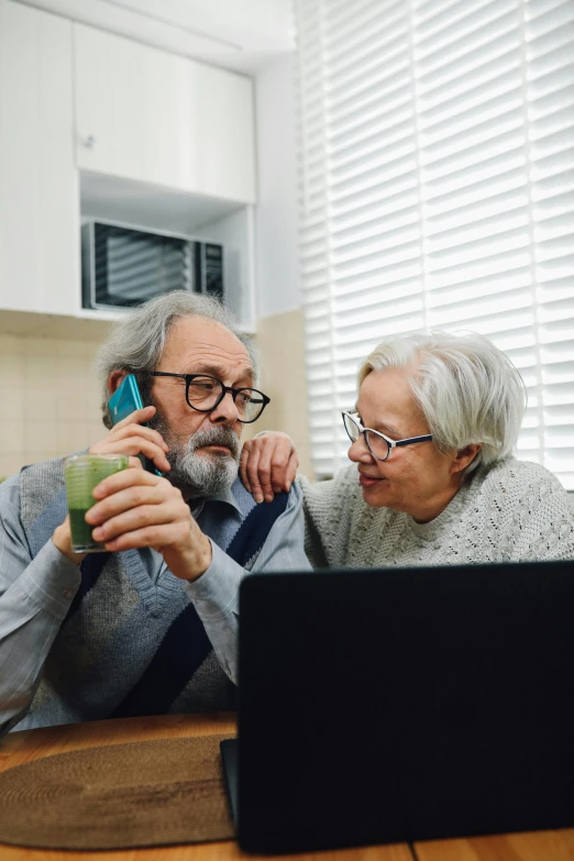 two people in front of a laptop using a cell phone