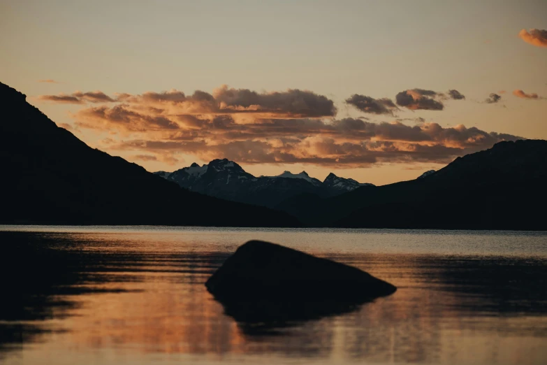 mountains reflecting in still water with a rock under the horizon