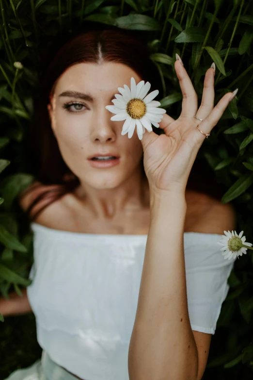 woman in white dress holding up one white flower to face