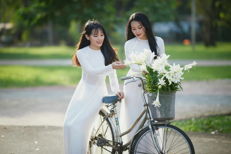 two young beautiful women standing next to a bicycle