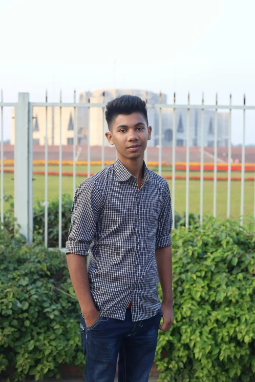 a boy wearing jeans standing by a fence