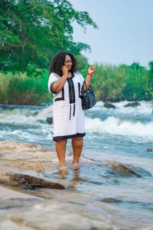 a black woman in a white dress stands on a river bank
